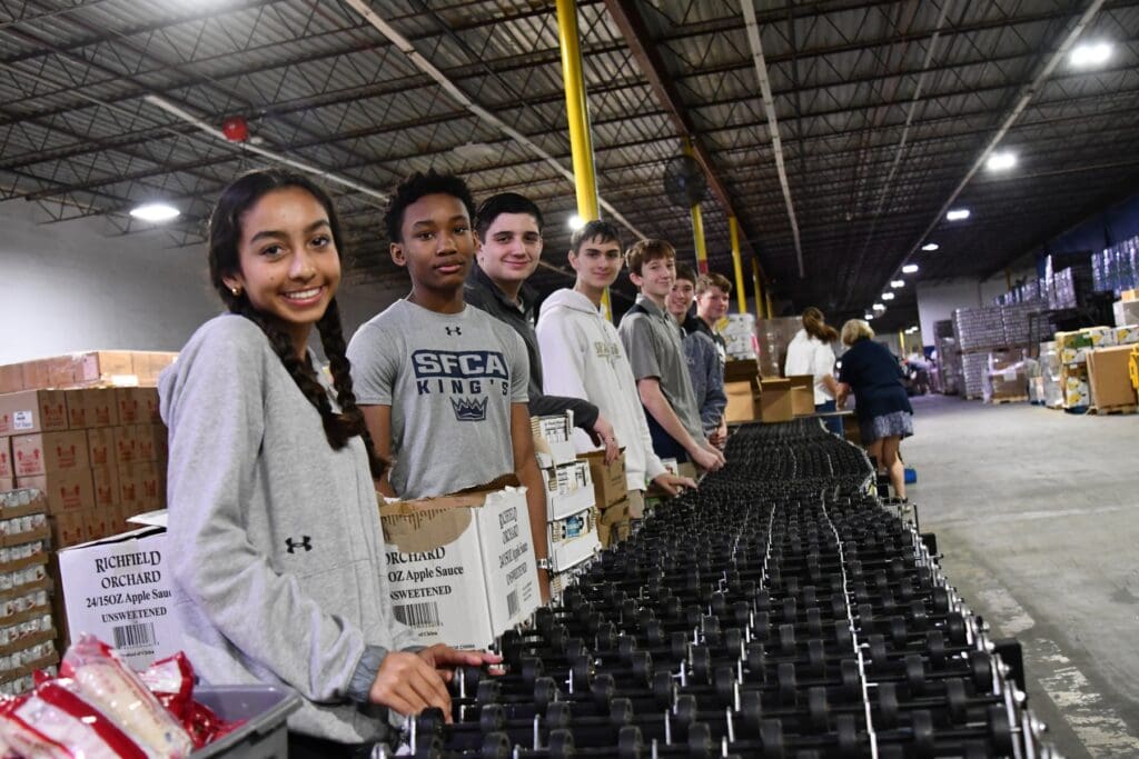 Students posing in front of an assembly line packing boxes